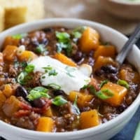 Bowl of butternut squash chili with beef, topped with sour cream, cilantro, and green onions.
