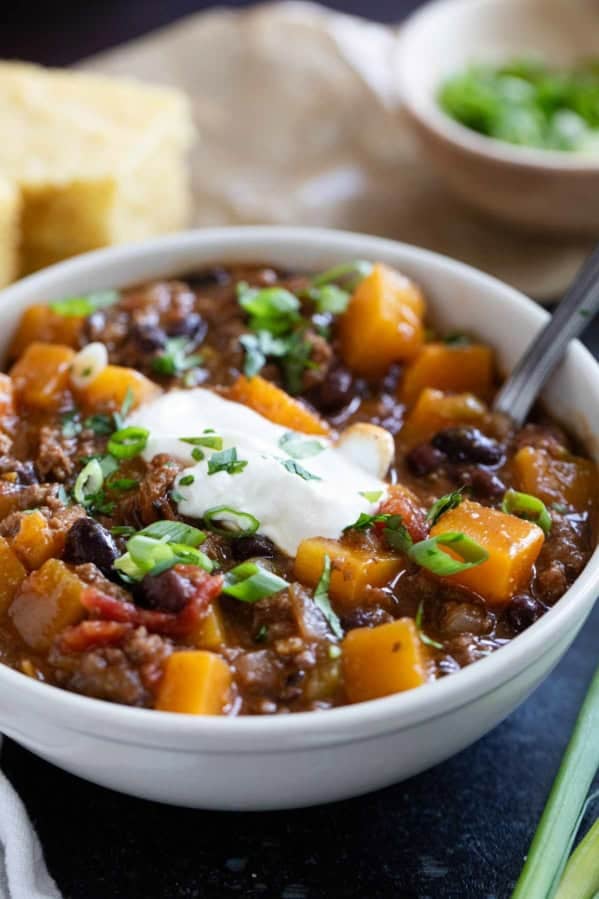 Bowl of butternut squash chili with beef, topped with sour cream, cilantro, and green onions.