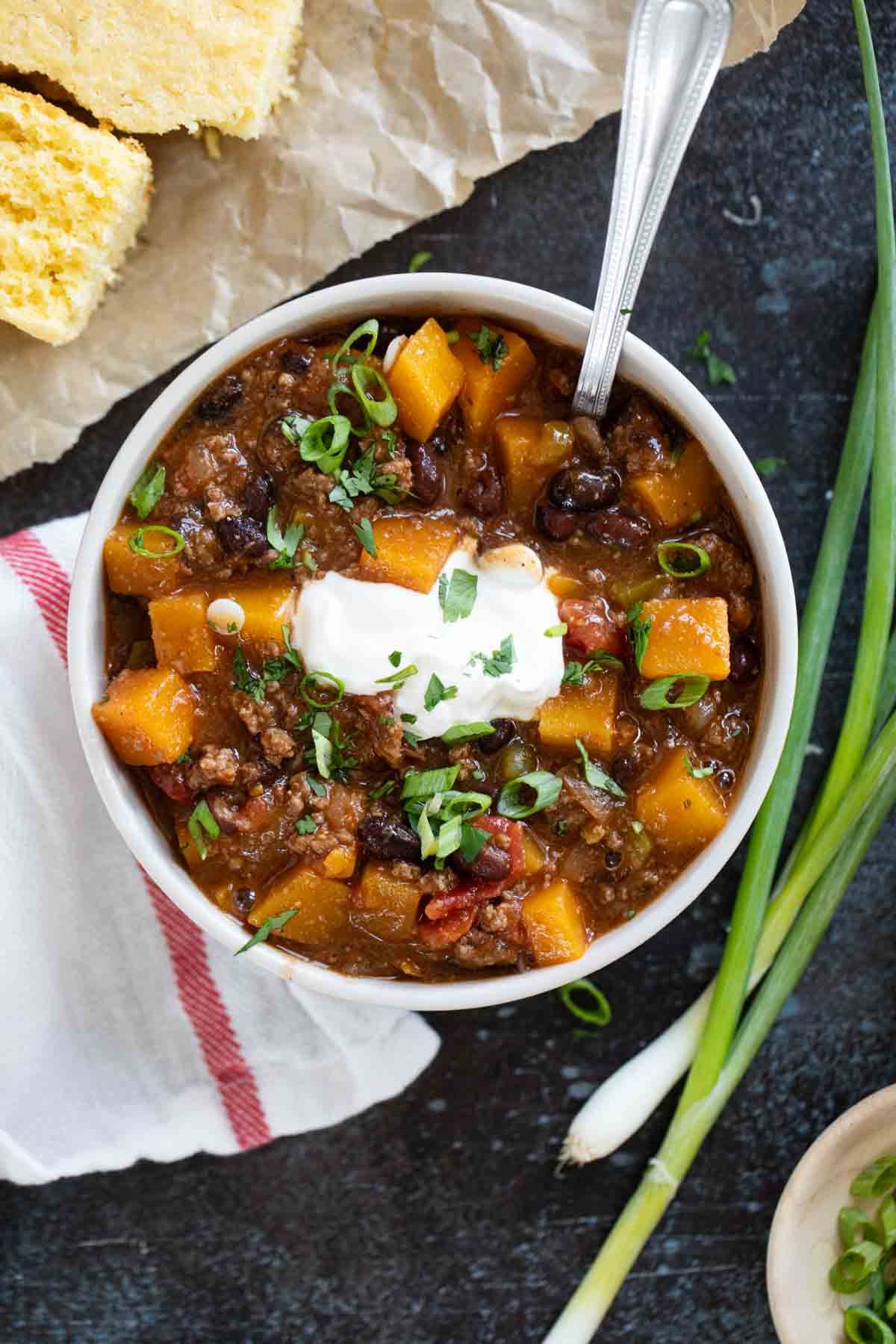 Bowl of Butternut Squash Chili with Beef, topped with sour cream and green onions.
