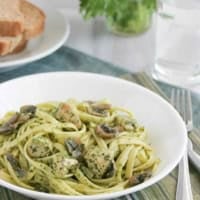 Serving of Chicken and Pasta with Cilantro Pesto in a white bowl, with bread and cilantro behind.