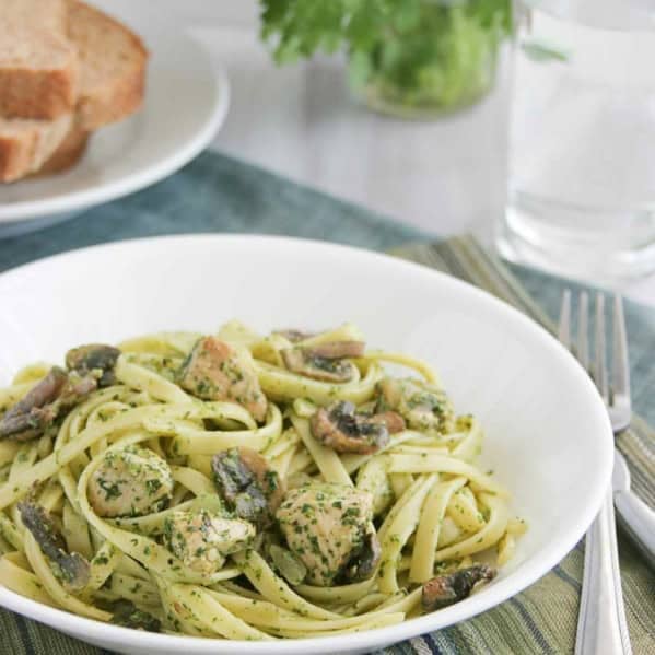 Serving of Chicken and Pasta with Cilantro Pesto in a white bowl, with bread and cilantro behind.