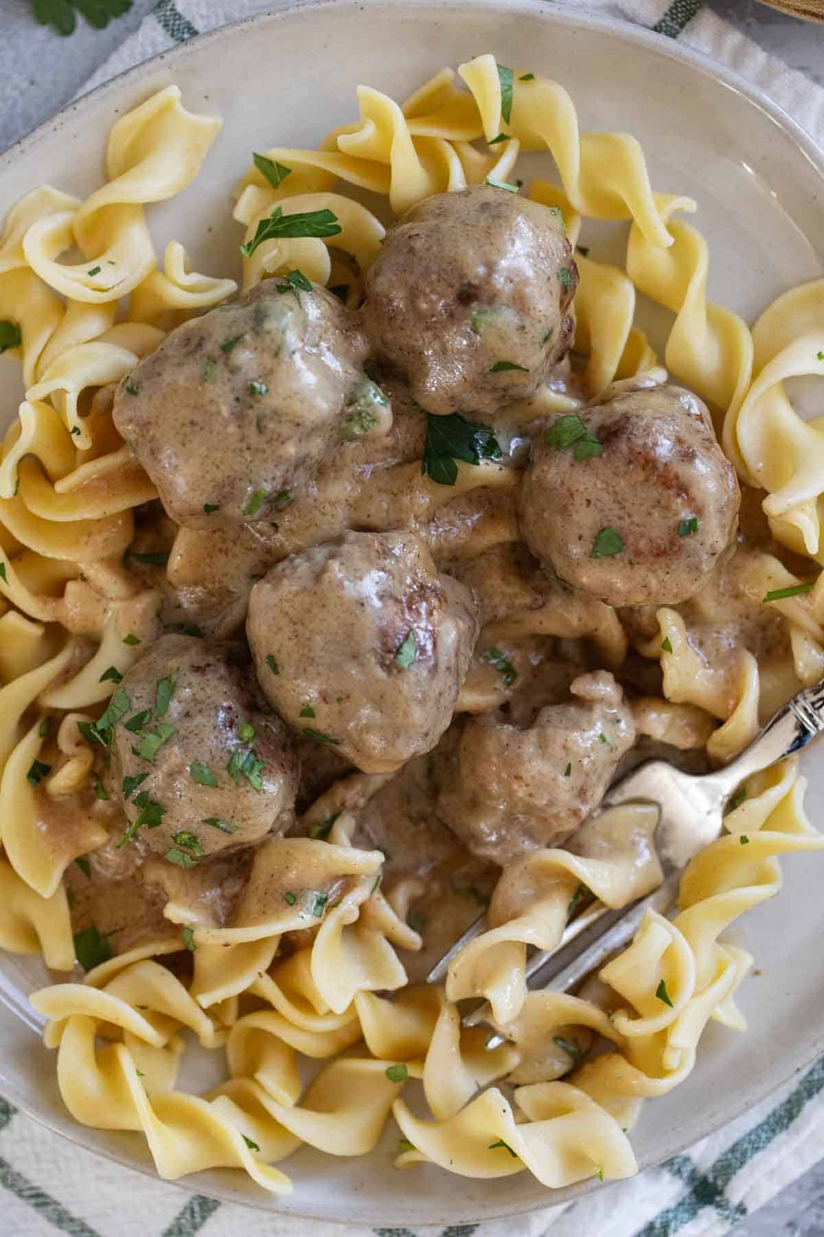 Swedish Meatballs over egg noodles on a plate with a fork.