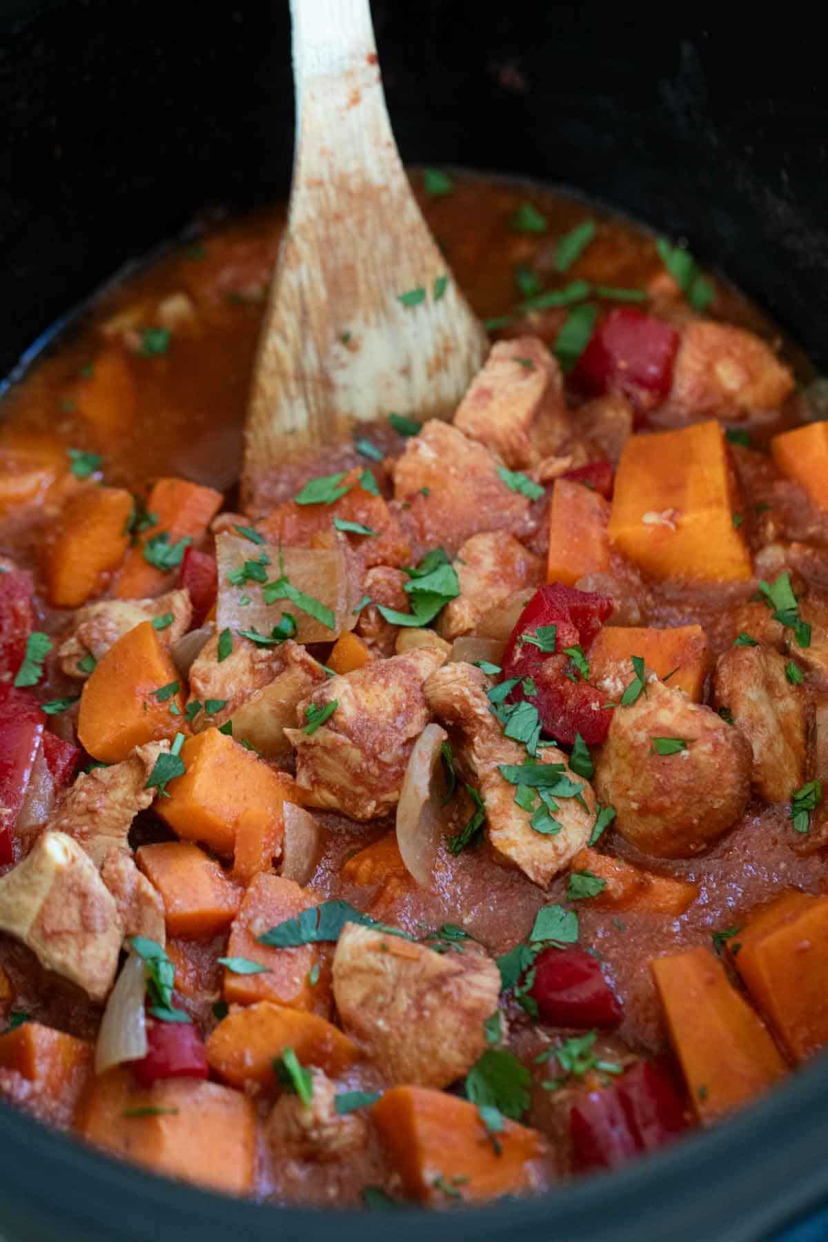 BBQ Chicken and Vegetables in a slow cooker with a wooden spoon for serving.