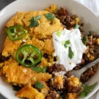 Chili Cornbread Casserole in a shallow dish, topped with sour cream, green onions, cilantro, and fresh jalapeño.