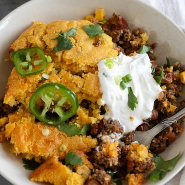 Chili Cornbread Casserole in a shallow dish, topped with sour cream, green onions, cilantro, and fresh jalapeño.