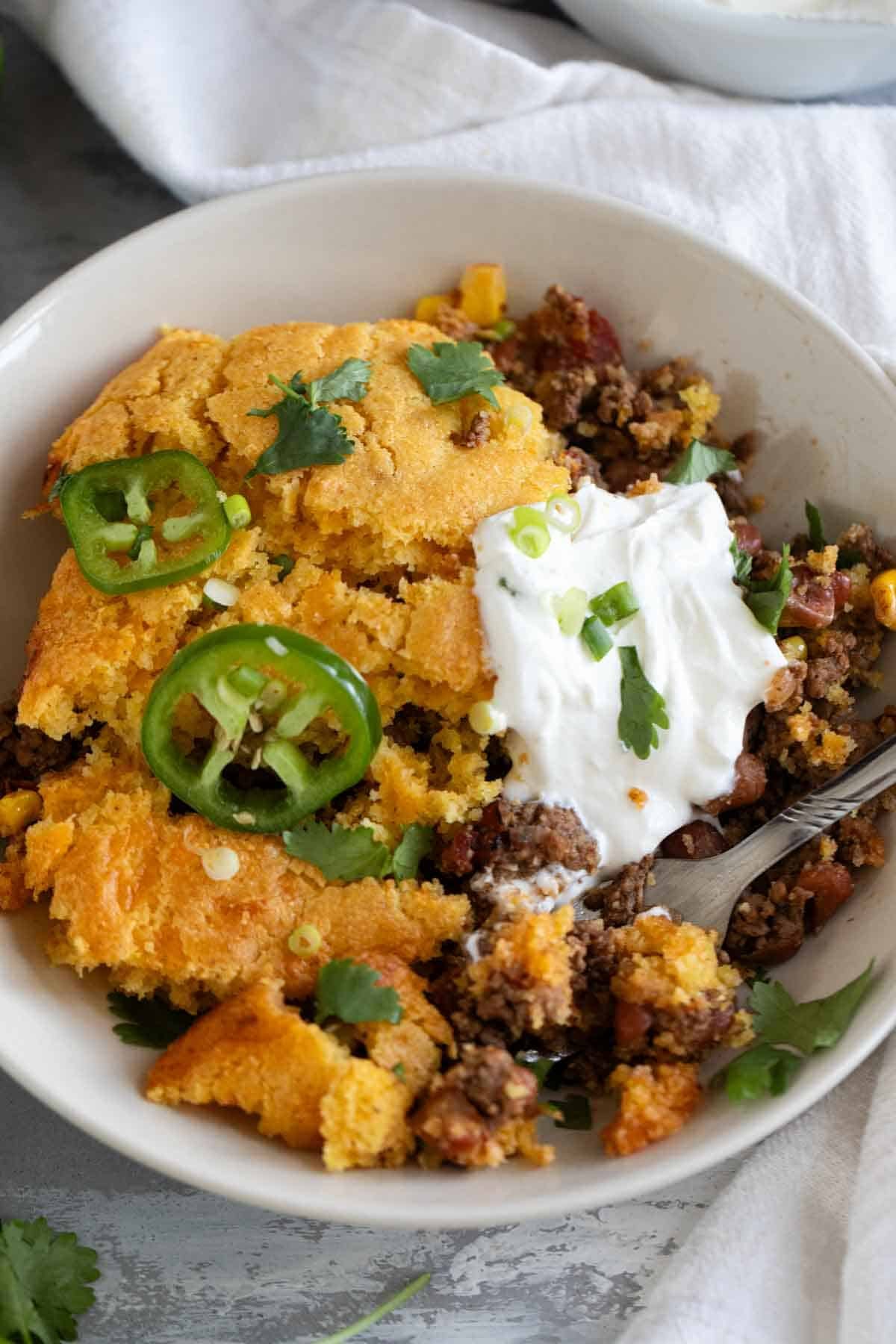 Chili Cornbread Casserole in a shallow dish, topped with sour cream, green onions, cilantro, and fresh jalapeño.