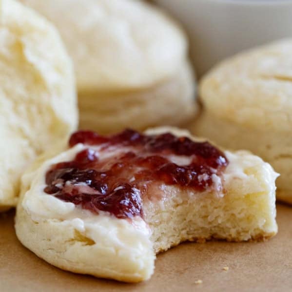 Cream biscuits topped with butter and jam, with a bite taken from it.