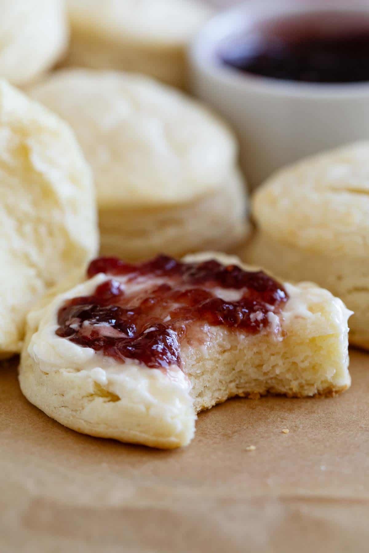 Cream biscuits topped with butter and jam, with a bite taken from it.