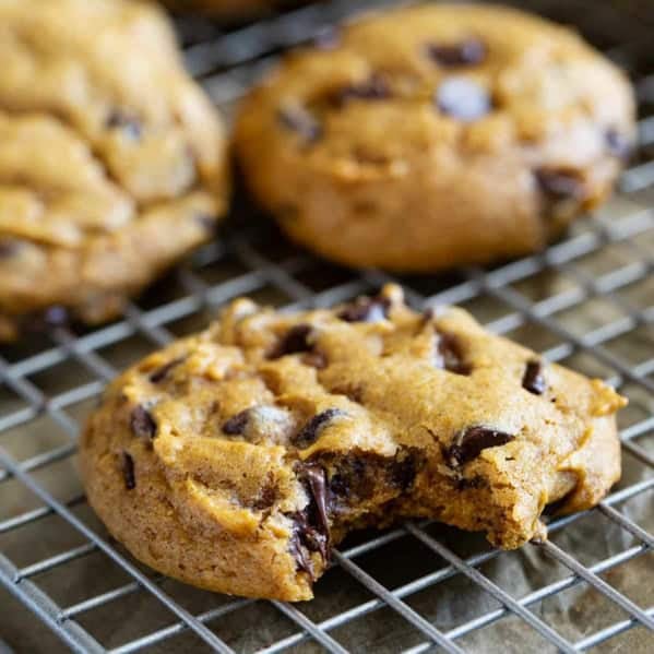 Pumpkin chocolate chip cookies on a cooling rack, with a bite taken from one.