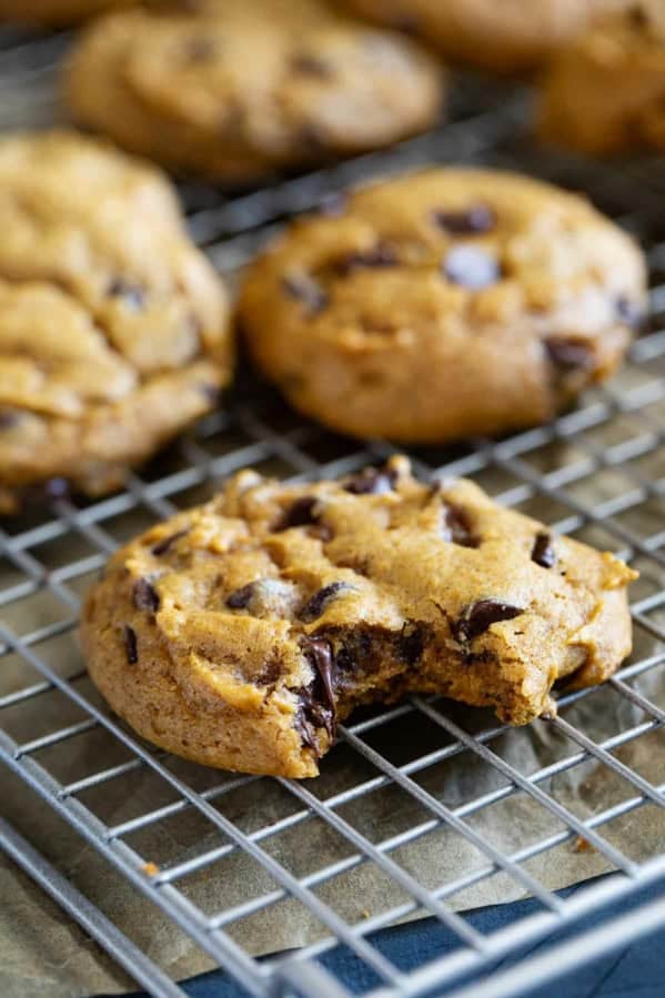 Pumpkin chocolate chip cookies on a cooling rack, with a bite taken from one.