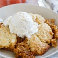 Serving of Pumpkin Cobbler in a bowl topped with vanilla ice cream.