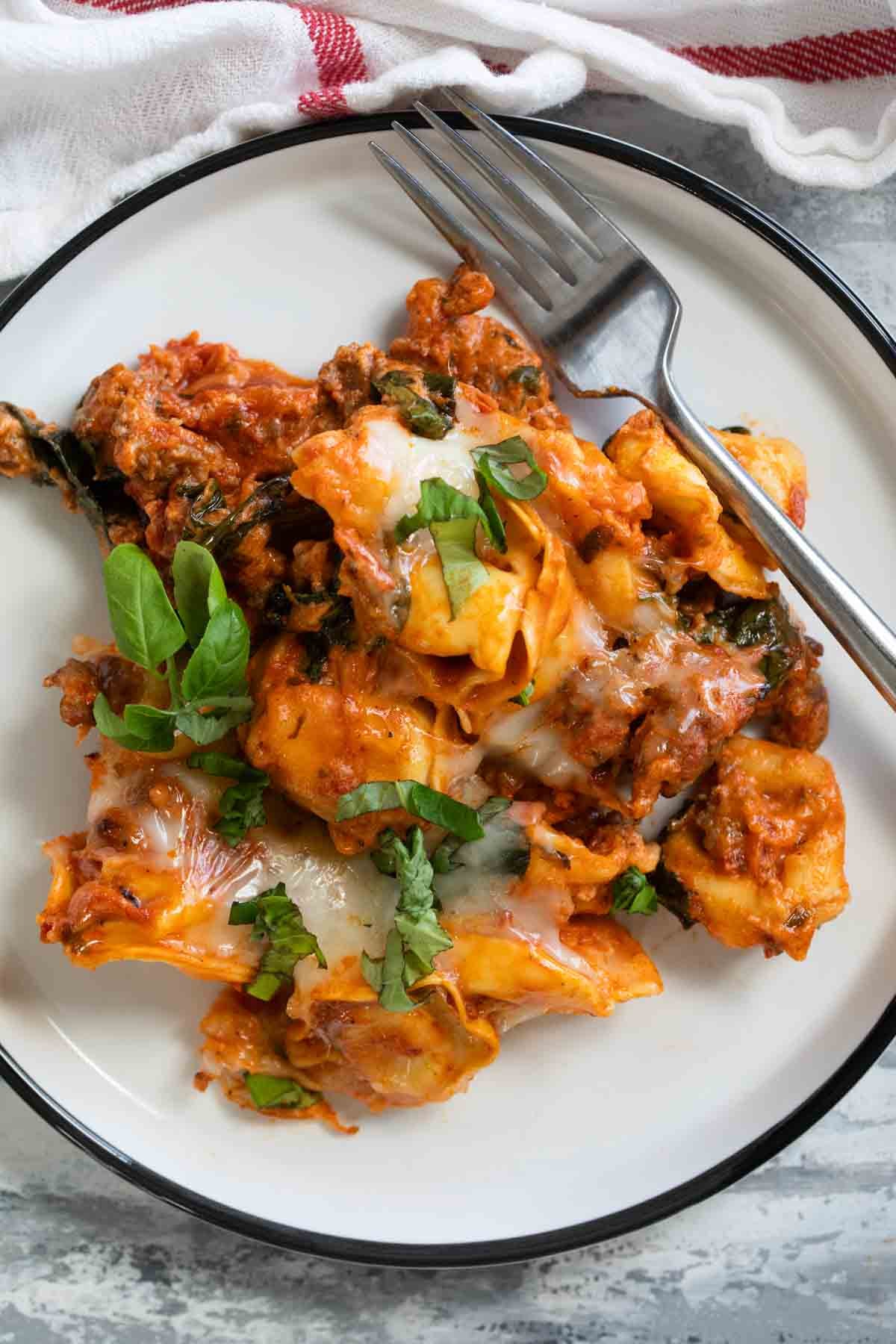 Serving of Sausage Tortellini Bake on a plate, topped with basil.